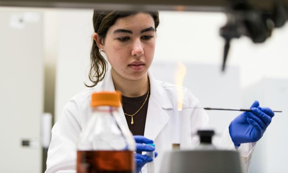 A female scientist in a lab coat conducts research in a laboratory at the University of Rochester.