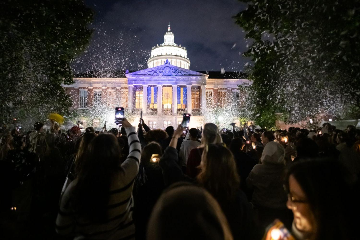 A group of individuals gathers outside the University of Rochester's capitol building, lighting candles in remembrance.